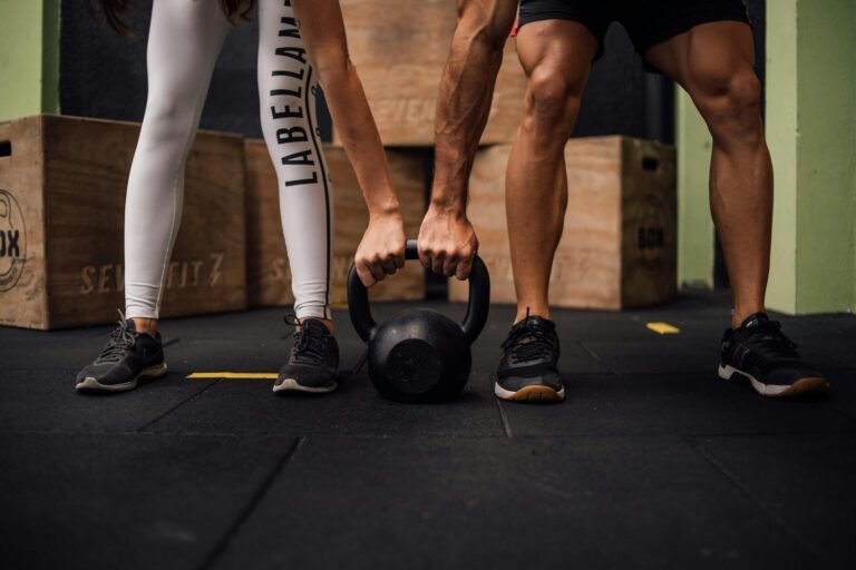 Hombre y mujer sujetando una kettlebell en el gimnasio, realizando ejercicio en conjunto