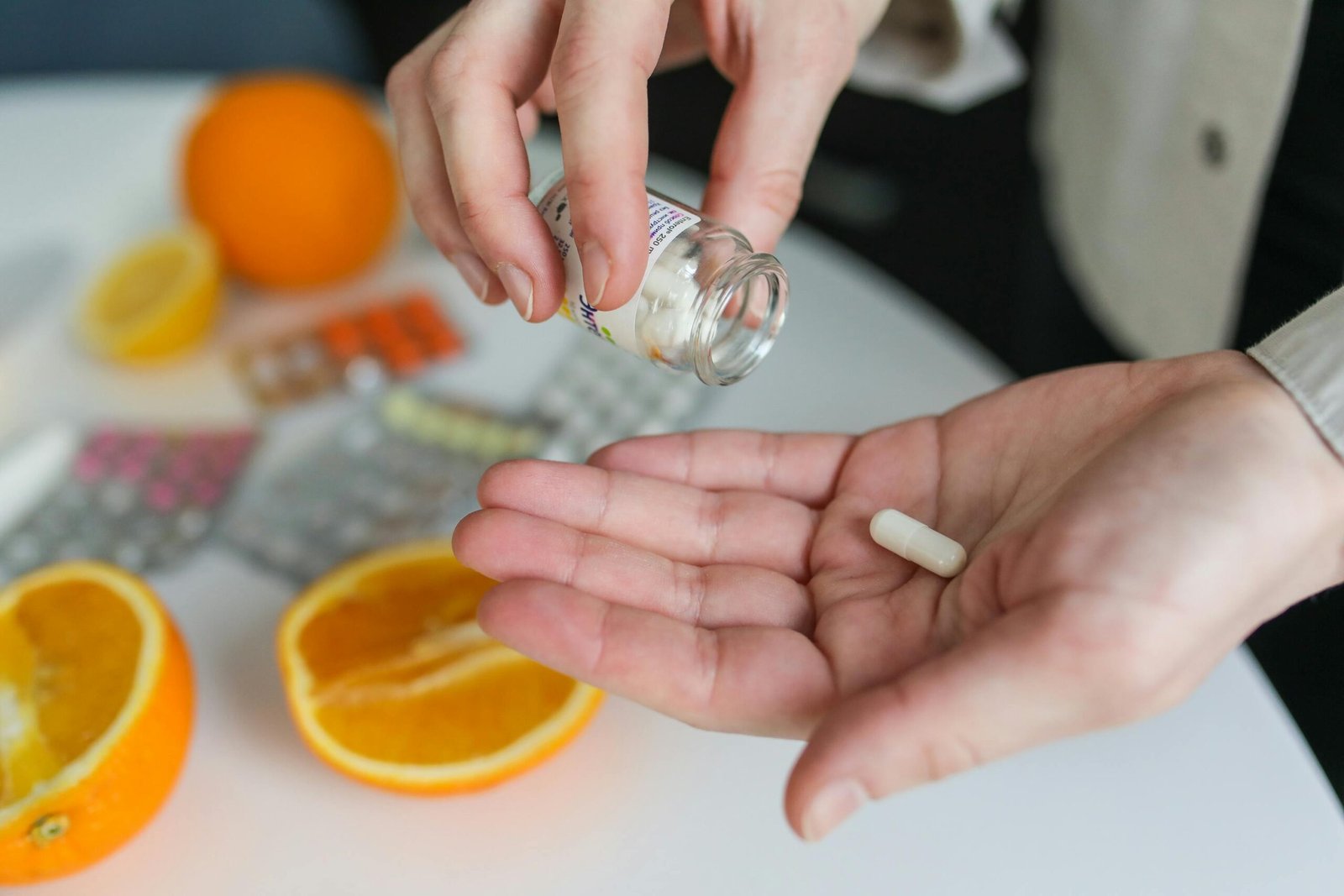 Persona tomando una cápsula de suplemento o vitamina con frutas y blísteres de pastillas en el fondo