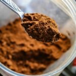 Cucharada de cacao puro en polvo en un recipiente, ideal para preparaciones saludables y recetas de chocolate