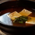 Sopa de miso tradicional japonesa con trozos de tofu y cebolleta en un cuenco oscuro