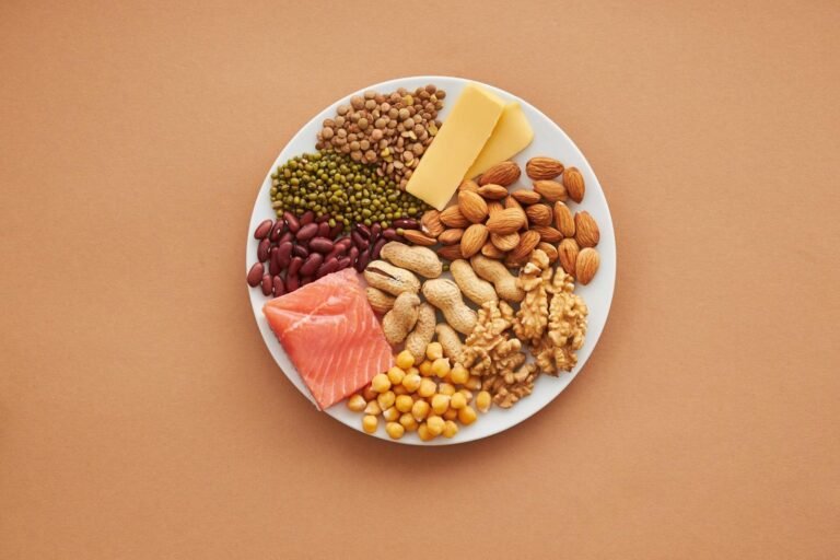 Plato con alimentos ricos en proteínas como salmón, nueces, almendras, legumbres y queso.