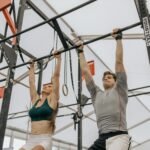 Hombre y mujer realizando ejercicios en barra en un gimnasio, representando entrenamiento funcional y fuerza.