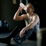 Hombre sentado en el gimnasio bebiendo agua después de un entrenamiento.