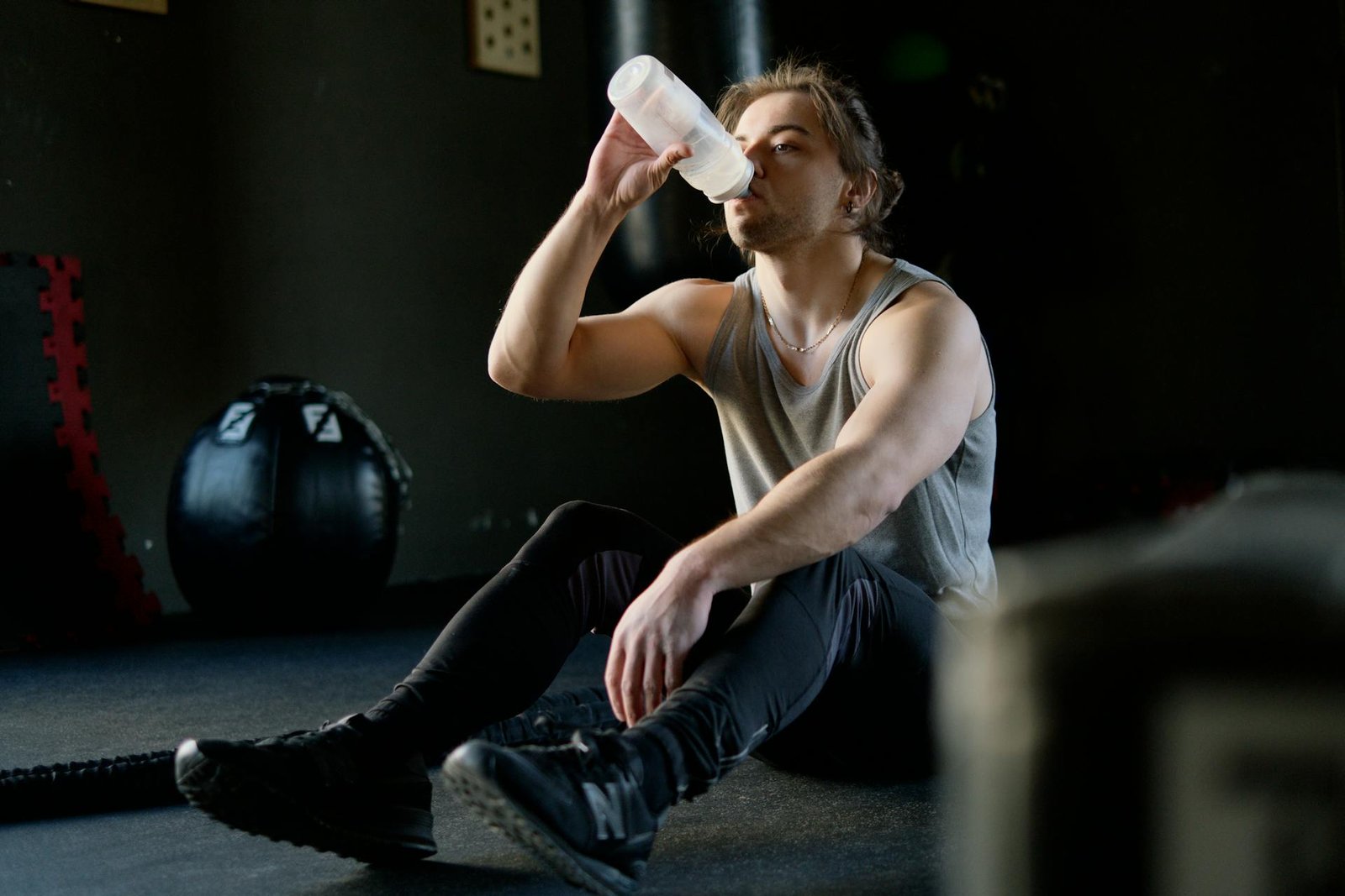 Hombre sentado en el gimnasio bebiendo agua después de un entrenamiento.