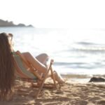 Mujer relajándose en una silla de playa frente al mar en un día soleado.