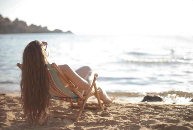 Mujer relajándose en una silla de playa frente al mar en un día soleado.