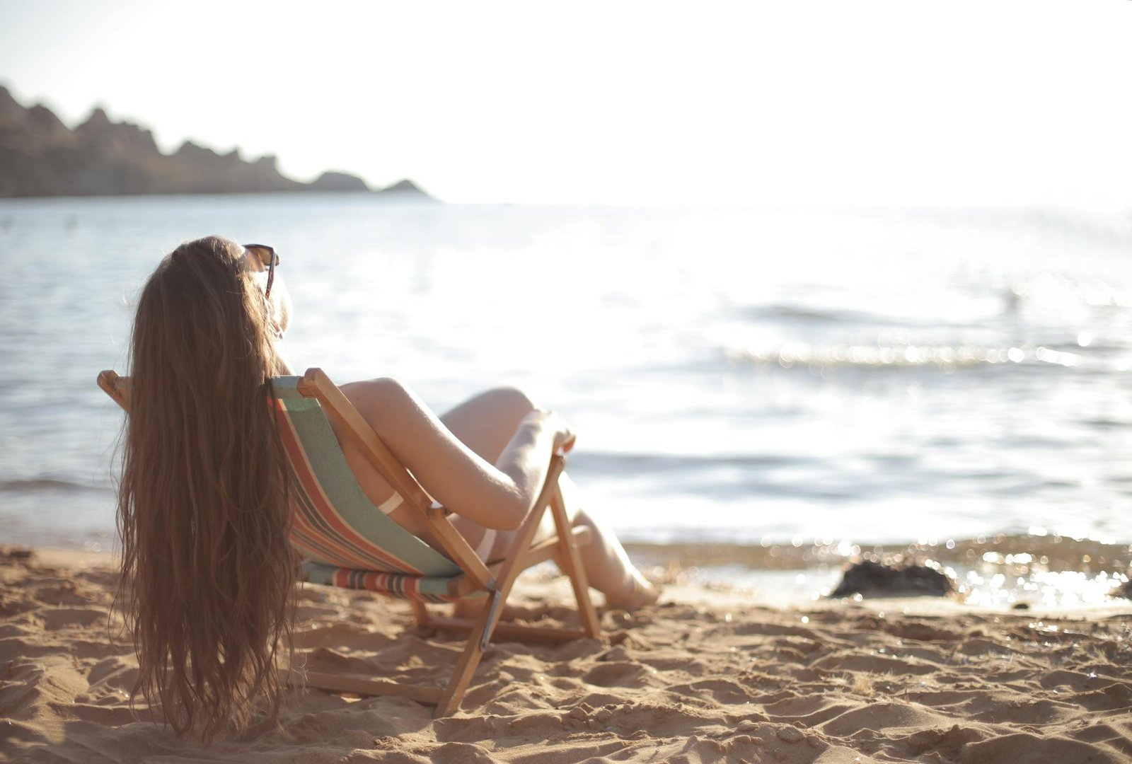 Mujer relajándose en una silla de playa frente al mar en un día soleado.