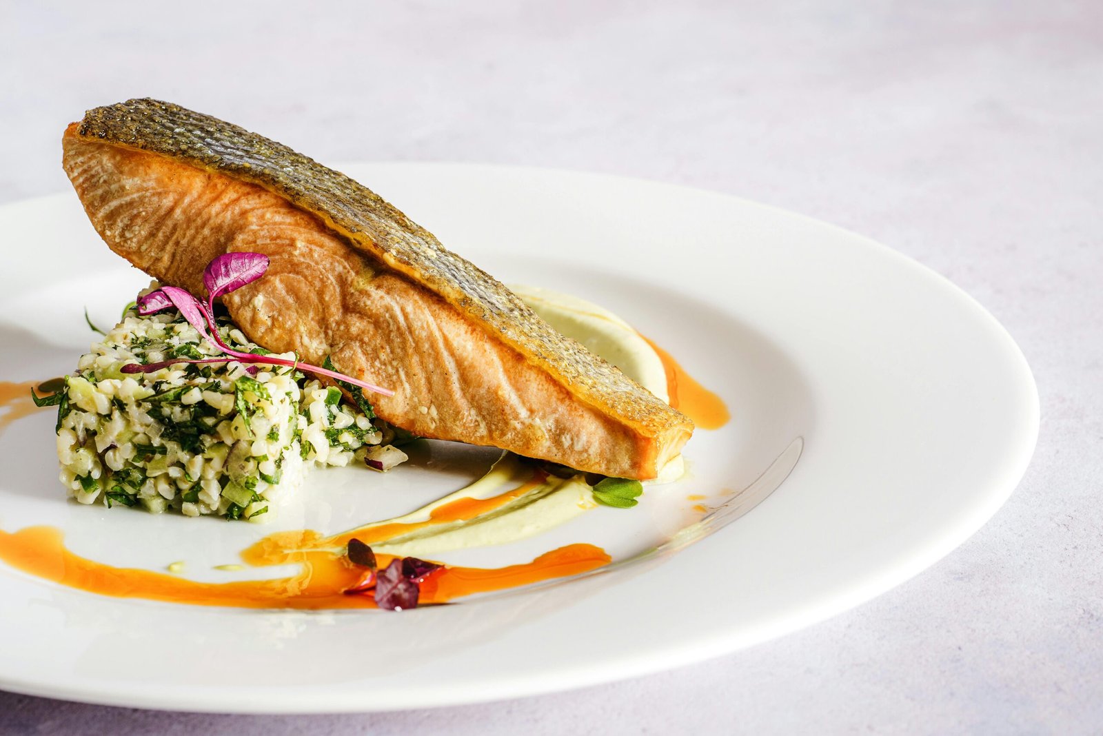 Plato de salmón gourmet con guarnición de granos y hierbas, servido con salsas decorativas en un plato blanco.