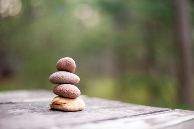 Cuatro piedras apiladas sobre una superficie de madera en un entorno natural.