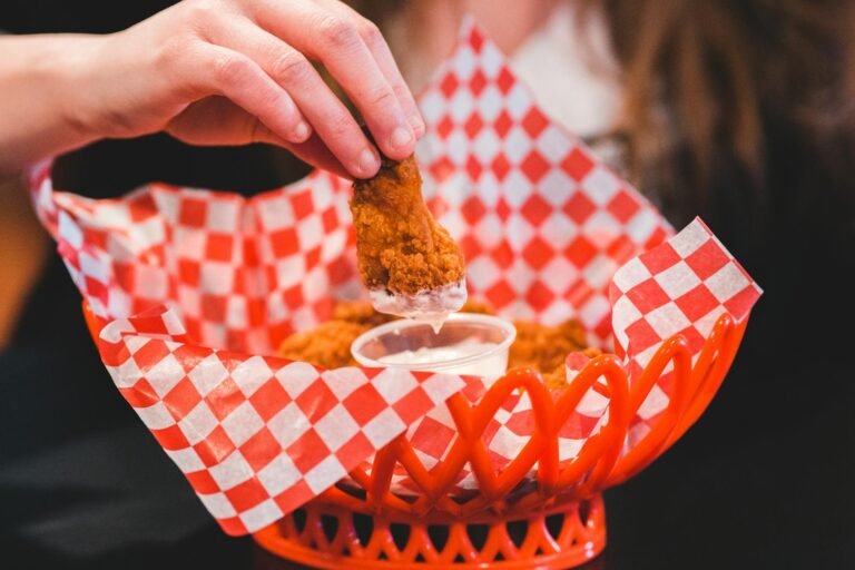 Alitas de pollo crujientes siendo sumergidas en aderezo, servidas en una canasta roja.