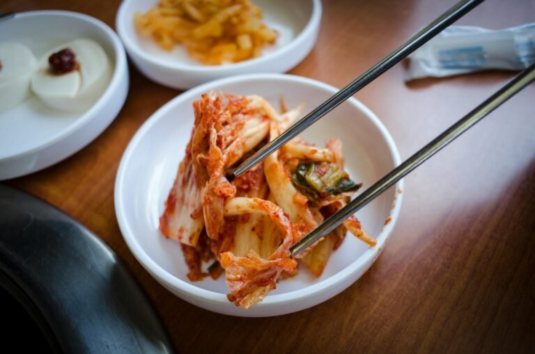 Plato de kimchi coreano tradicional servido en un recipiente blanco con palillos.