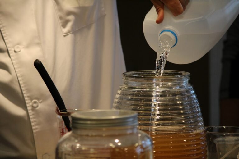 Preparación artesanal de kombucha, vertiendo agua en un recipiente de vidrio en un ambiente de cocina.