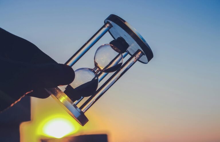 Silueta de un reloj de arena contra un cielo al atardecer, simbolizando el paso del tiempo.