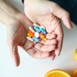 plano cercano de manos sosteniendo cápsulas multicolores y naranjas sobre una mesa, simbolizando salud y nutrición