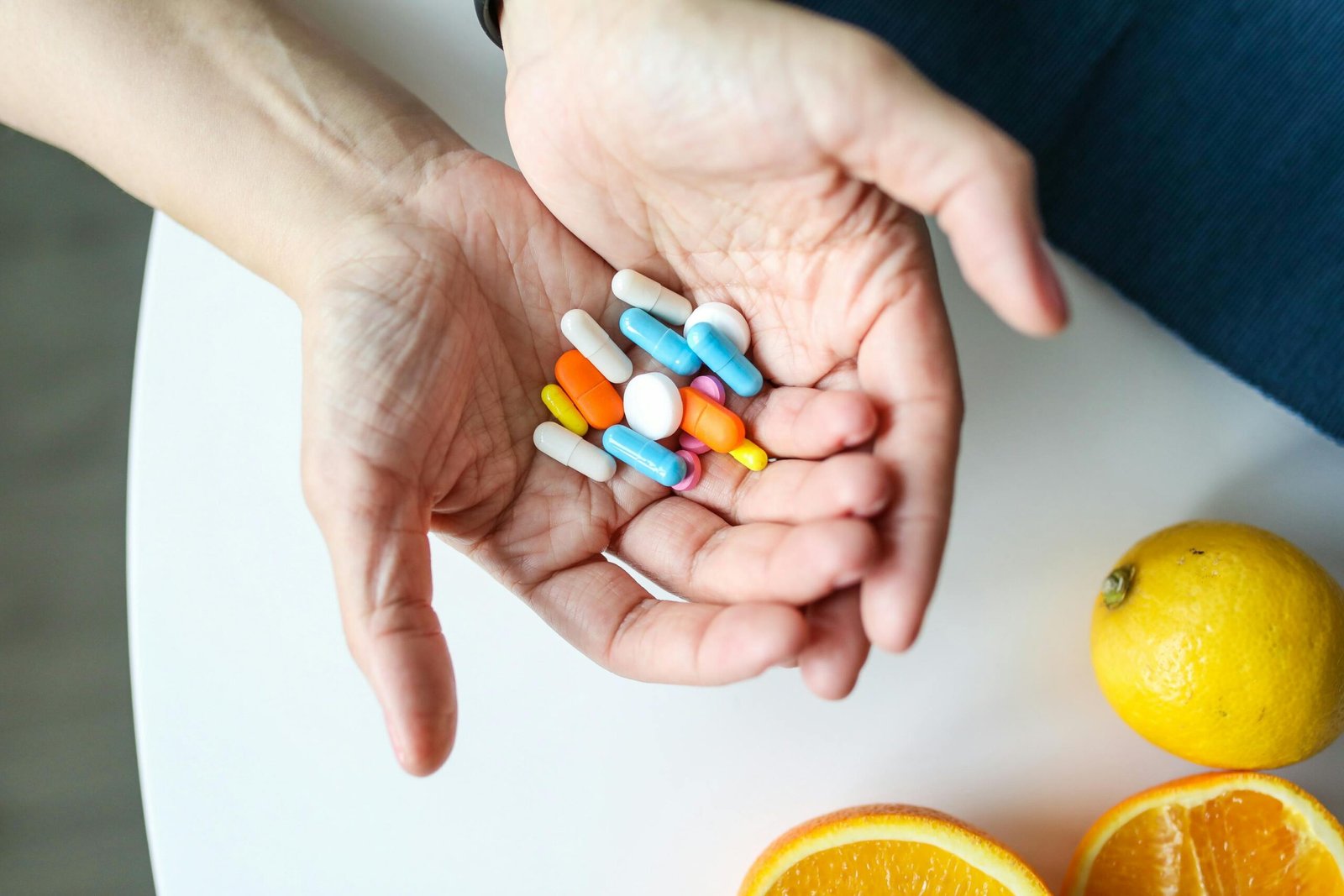 plano cercano de manos sosteniendo cápsulas multicolores y naranjas sobre una mesa, simbolizando salud y nutrición