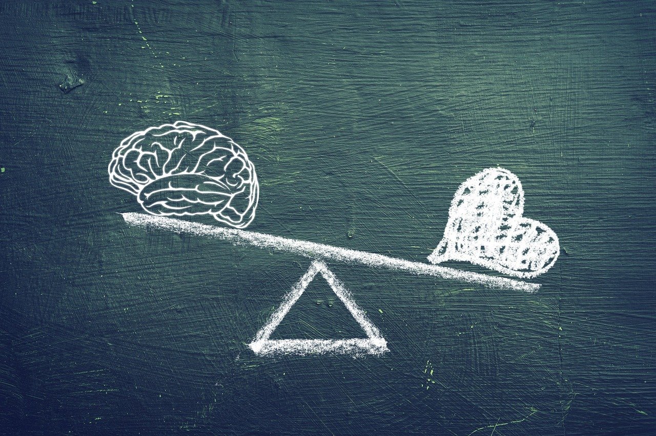 representación de un cerebro y un corazón en extremos opuestos de una balanza, dibujados en tiza sobre una superficie de pizarra.