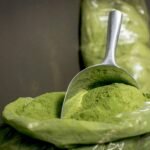 Primer plano de polvo de moringa fresco en una cuchara de acero inoxidable, resaltando su vibrante color verde.