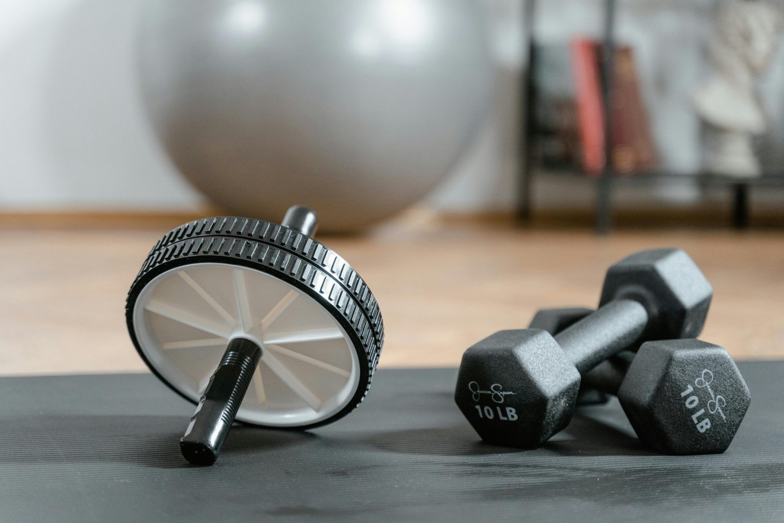 Primer plano de una rueda abdominal y mancuernas sobre una colchoneta en un gimnasio en casa.